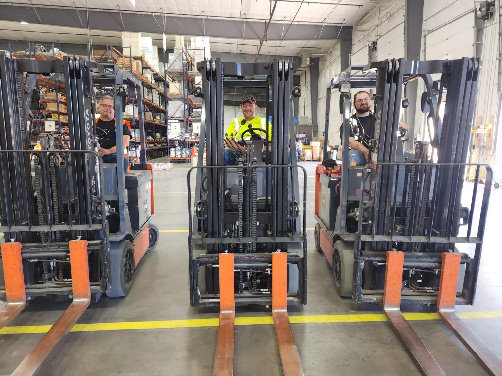 Three men on forklifts smiling at the camera